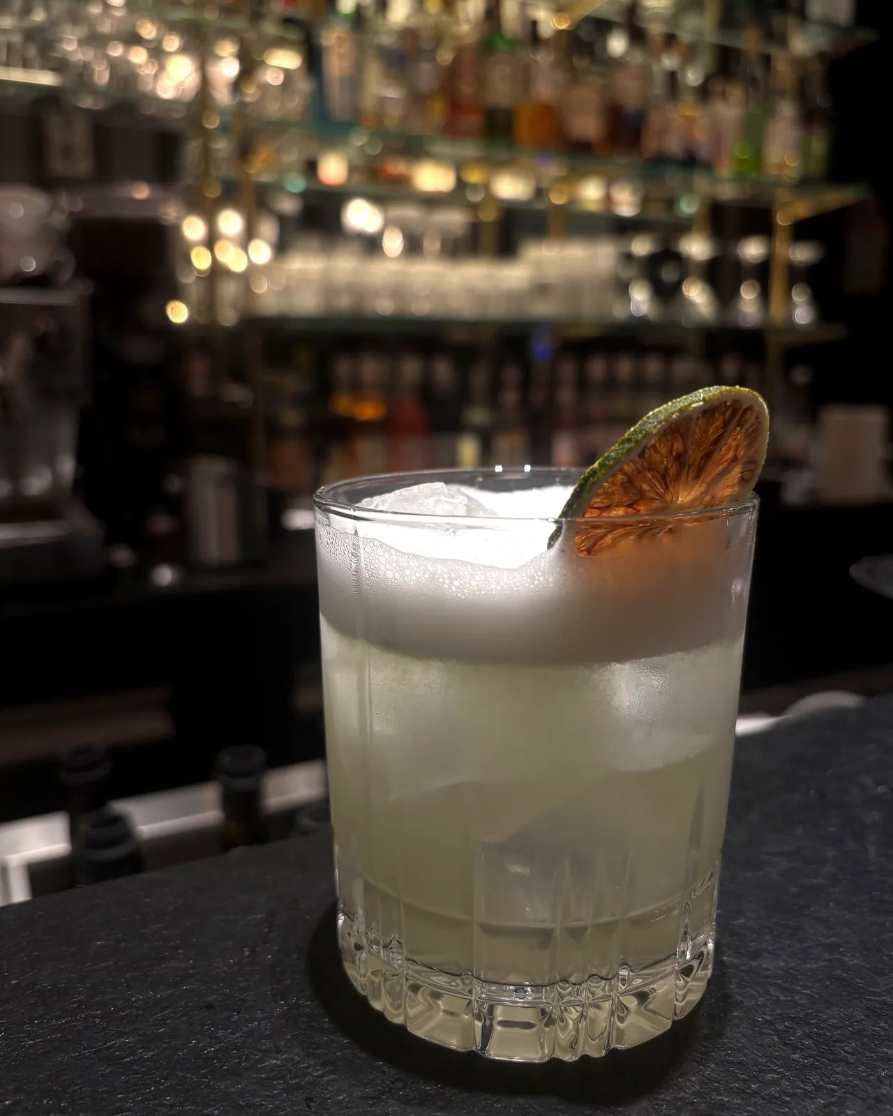 Cocktail jaune pâle sur glaçon unique, rondelle de citron vert séchée en garniture.